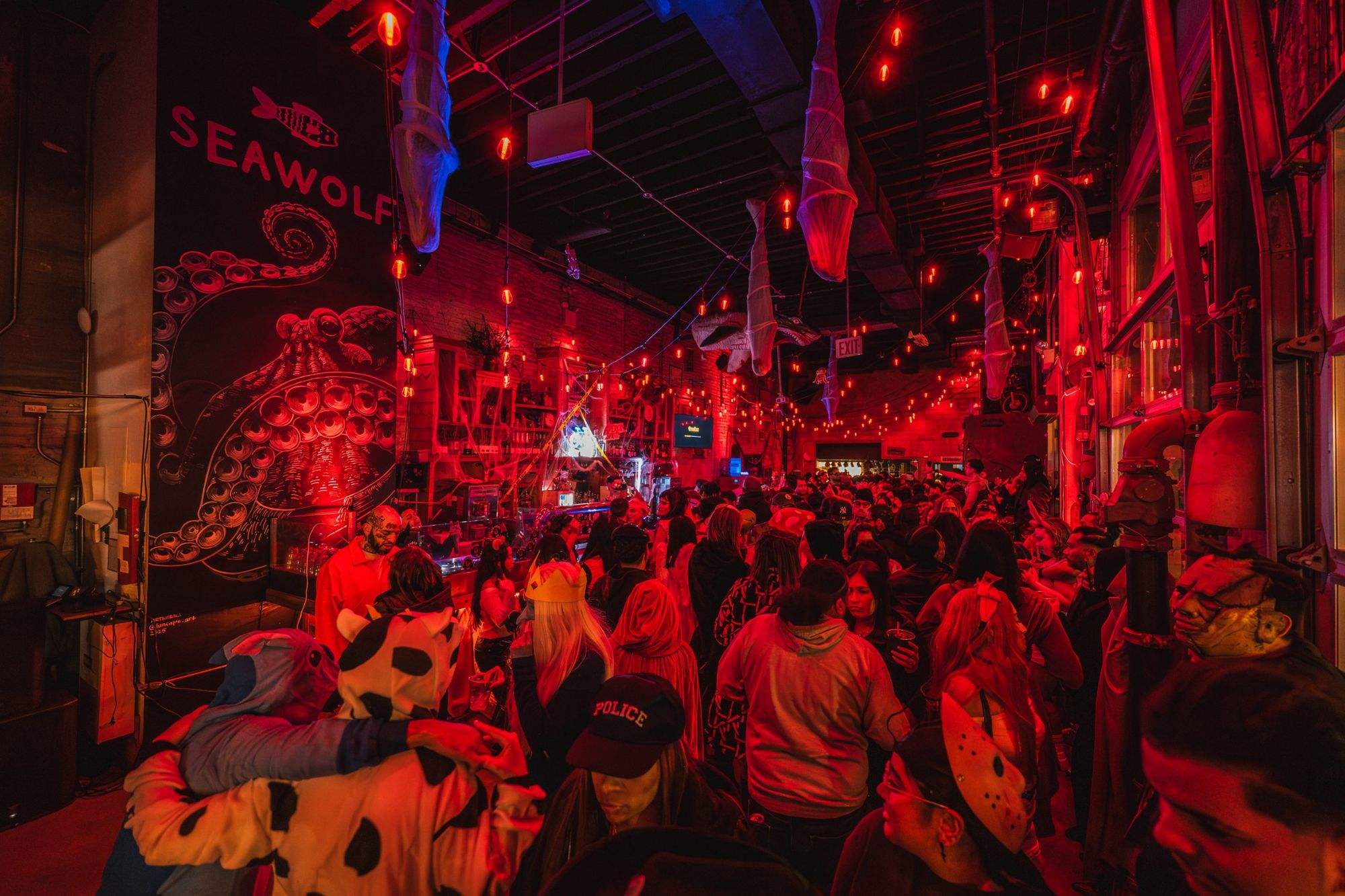A packed Sea Wolf night: red light, the octopus mural and a crowd in costume at the bar